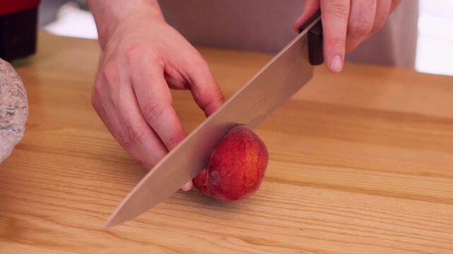 Slicing nectarine. Fresh fruit preparing. Unrecognizable professional man chef hands using knife on wooden board making natural dessert in kitchen.
