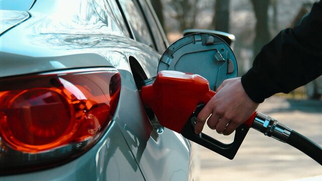 Fueling a car at a gas station, close-up of a man's hand holding a fuel nozzle at the gas tank.