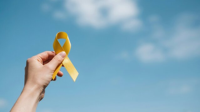 Hand holding yellow ribbon against a blue sky background for suicide prevention awareness