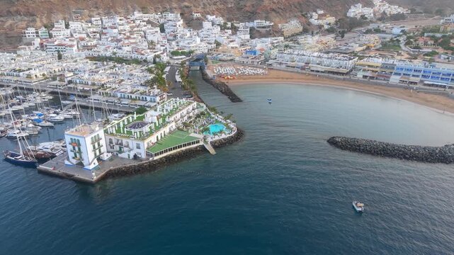 Beautiful aerial perspective of the charming port and beach of Mogan in Gran Canaria. The camera captures the coastal village and marina