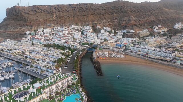 Picturesque aerial establishing shot of the Puerto de Mogan marina and village in Gran Canaria at sunrise, revealing the beach and boats