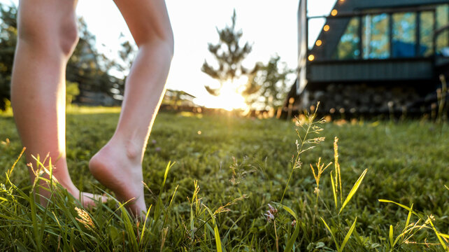 Barefoot person walking on grass at sunset near a glamping tent