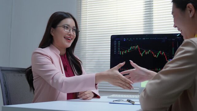 Financial advisor discussing investment strategy and stock market trends with her smiling asian client and shaking hands