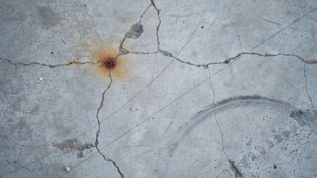 Cracked grey concrete floor surface with a central rust stain and a faint circular tire mark