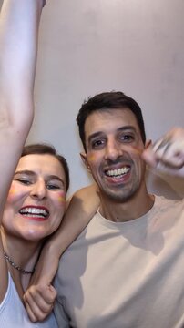 Cheerful Spanish Couple Fans with Flag Face Paint Cheering and Supporting Spain Team Before Match. Happy Friends Supporters Celebrating Victory or Goal Indoors. (187 characters)