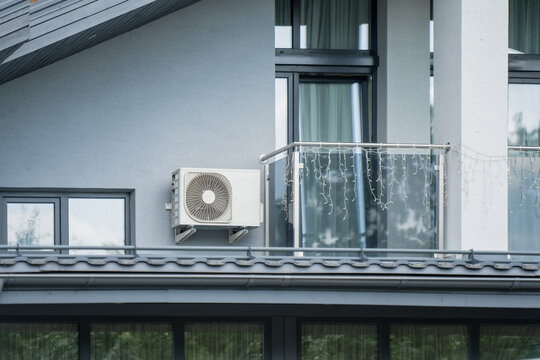 Outdoor air conditioner compressor unit installed on a residential house wall next to a modern balcony representing HVAC appliance setup