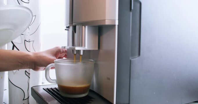 Coffee making. Drink preparing. Female hands using automatic espresso machine for fresh morning beverage at home kitchen indoor.
