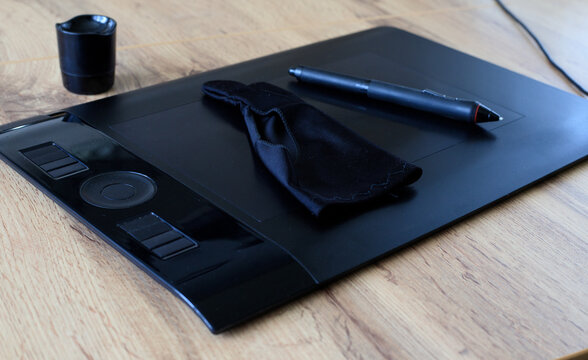Digital stylus and a black drawing glove rest on a black graphics tablet. Digital illustration process