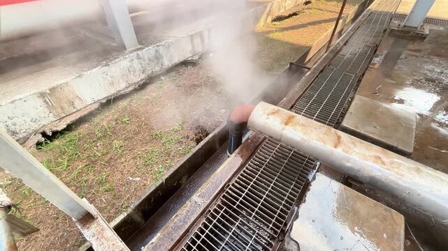 Steam vents from industrial pipe onto wet grating