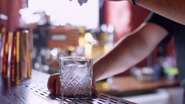Cool beverage preparing. Ice cube mixing. Unrecognizable barman hand stirring alcohol drink with professional spoon in transparent glass on bar counter.
