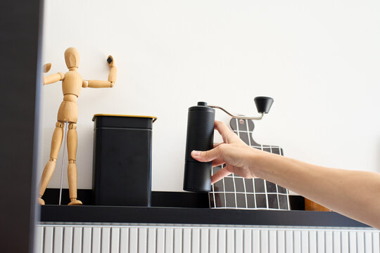 Hand takes manual coffee grinder from kitchen shelf before brewing coffee