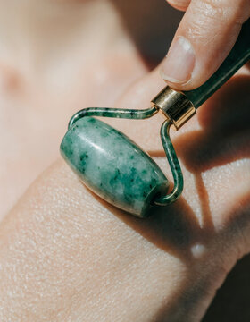 Green jade facial roller hand skincare massage wellness beauty self care relaxation closeup natural stone hand gently rolling green jade facial roller skin promoting relaxation and wellness