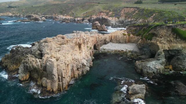 Aerial drone footage of the dramatic coastline at Point Lobos in Big Sur, California. The shot captures rugged cliffs, turquoise Pacific Ocean waves, rocky coves, and untouched natural landscapes.