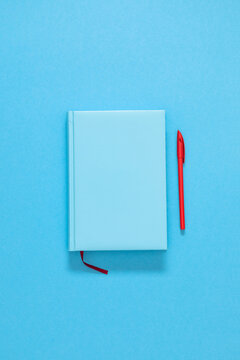 Closed blue notebook diary with red pen on bright blue background. Minimalist business mockup template with wide copy space, education planner background, school stationery layout, flat lay.