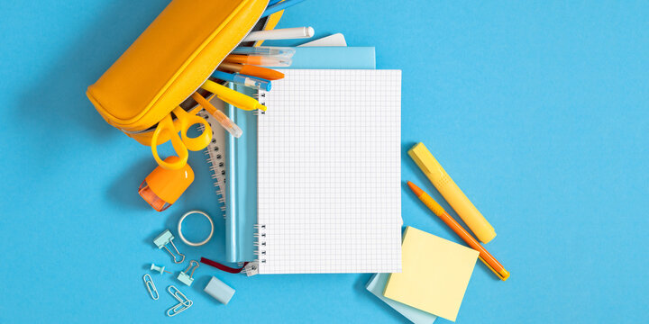 Open blank notebook with yellow pencil case and school stationery on blue background. Back to school banner template with copy space, education concept layout, student desk flat lay background.
