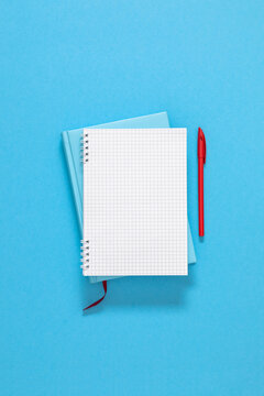 Open blank grid notebook on closed blue diary with red pen. Minimalist business mockup template with wide copy space, education planner background, school stationery layout, vertical flat lay.