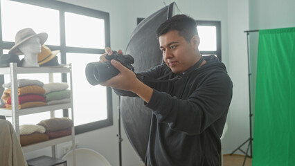 Fototapeta premium Man holding camera and adjusting lens in studio with green screen and reflector; creative concentration.