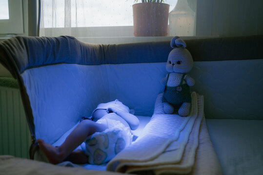 Newborn resting in a medical crib under blue light phototherapy for jaundice, wearing eye protection with a teddy bear nearbyneonatal care and gentle recovery in hospital