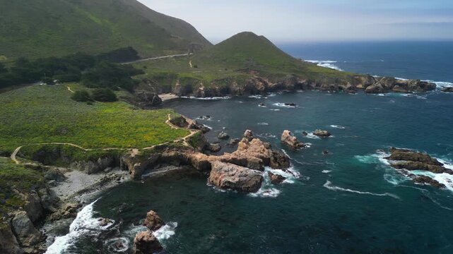 Aerial drone footage of the dramatic coastline at Point Lobos in Big Sur, California. The shot captures rugged cliffs, turquoise Pacific Ocean waves, rocky coves, and untouched natural landscapes.