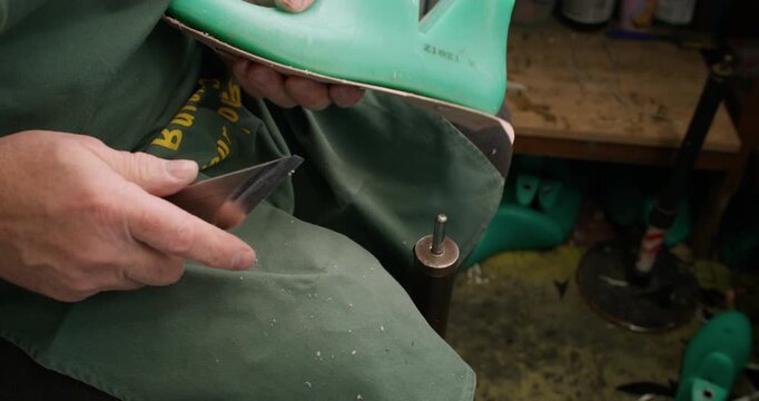 Shoemaker workshop. Handmade footwear. Unrecognizable tailor man hands cutting shaping insole on wooden shoe last using knife at workspace.
