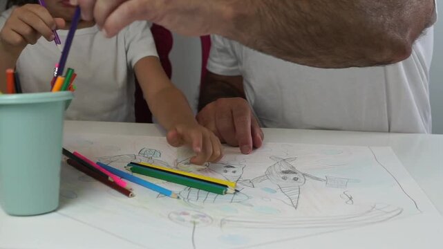 Un padre y su hija peque&ntilde;a seleccionan y colocan l&aacute;pices de colores en un vaso de pl&aacute;stico sobre un dibujo de un animal marino, prepar&aacute;ndose para una actividad art&iacute;stica en casa.