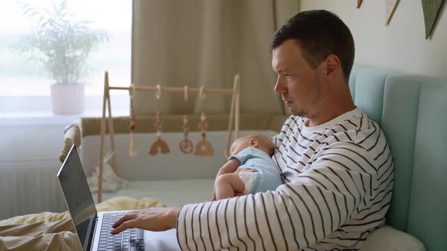 Young, exhausted father holding a sleeping newborn while working on a laptop from his bed, facing the challenges of multitasking, sleep deprivation, and remote work on paternity leave