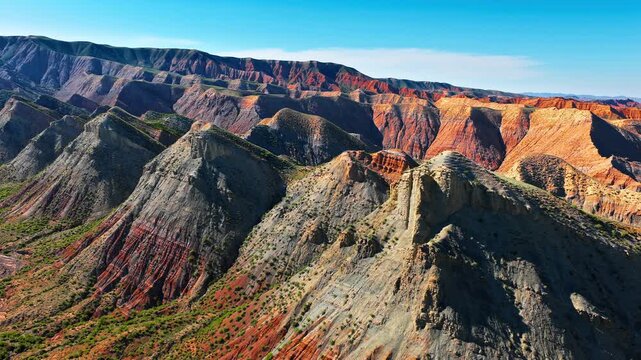 Aerial view of multi-colored mountain peaks with unique geological strata under a clear blue sky in Xinjiang, China. Perfect for travel, geography, and nature themes.