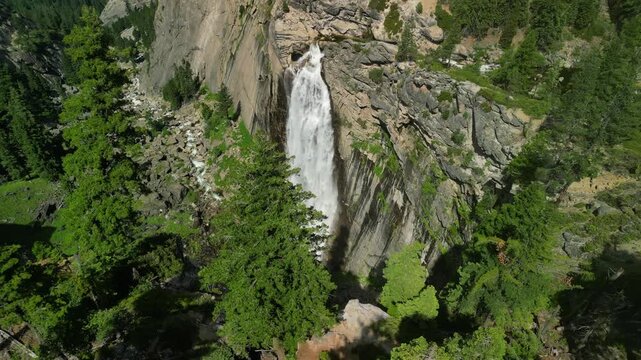 Aerial shot of Yosemite Valley featuring cascading waterfall surrounded by granite cliffs, dense forest, and dramatic mountain landscape in California&rsquo;s Sierra Nevada.
