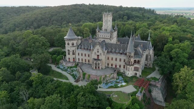 Marienburg Castle and its Gothic Revival facade surrounded by forest reverse aerial