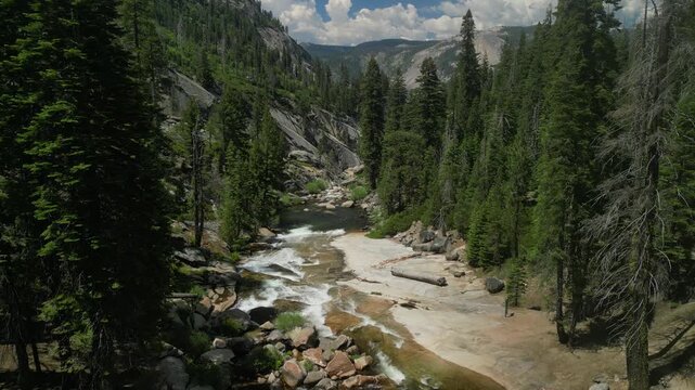 Aerial shot of Yosemite Valley featuring cascading waterfall surrounded by granite cliffs, dense forest, and dramatic mountain landscape in California&rsquo;s Sierra Nevada.
