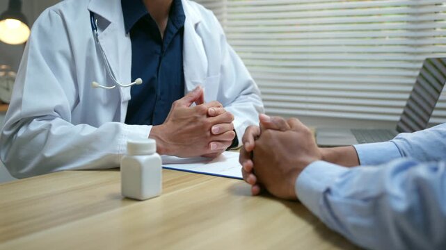 Compassionate doctor comforting a worried patient by holding his hands in a medical office while giving bad news