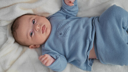 Newborn baby on bed in blue knit outfit reaches hand and gazes upward toward a soft mobile, showing tiny hand and relaxed face  serenity and wonder. © Krakenimages.com
