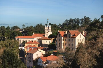 Obraz premium Charming buildings with orange rooftops rise against the lush backdrop of Sintra, Portugal