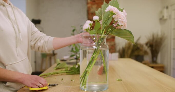 Floral composition. Bouquet arrangement. Unrecognizable female florist cutting flowers placing hydrangea in glass vase for home decoration.