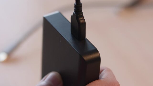 Hand steadies matte black adapter while micro usb cable seats into recessed top port, showing clean indoor technology connection with soft warm blur and tight closeup detail
