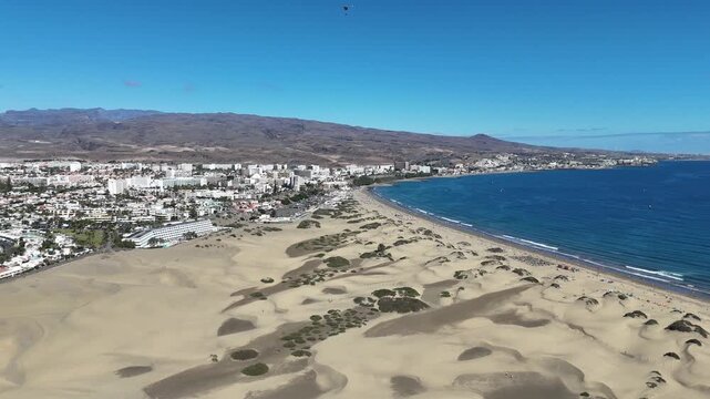 Aerial panorama flight over Maspalomas Dunes with hotels in Playa del Ingles, beach, Atlantic ocean, mountains and paraglider on Canary Island Gran Canaria, Spain