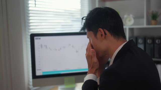 Stressed businessman feeling tired while trading online on his computer losing money in a declining stock market