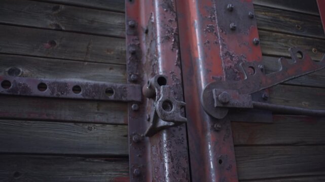 Weathered red metal hinge and latch on dark wooden planks, showing rust, peeling paint, rivets, corroded steel, rustic industrial texture and worn surface detail