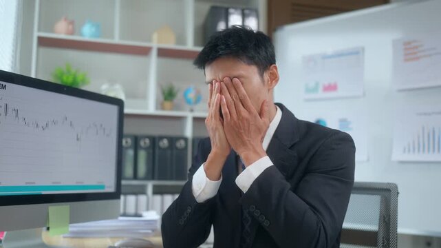 Stressed asian businessman feeling despair after financial loss watching a falling stock market chart on a computer