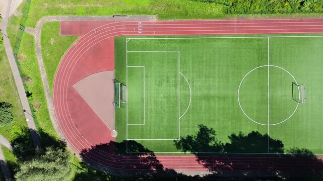 Top down drone shot of green football field and red running track stadium