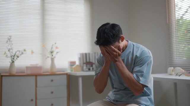 Stressed asian man suffering from depression and mental health issues feeling anxious and alone in his apartment at home