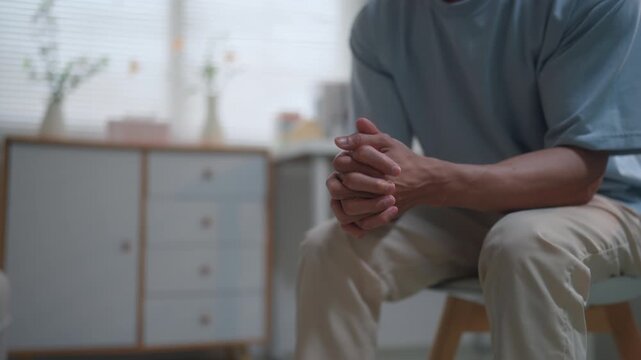 Worried man wringing hands showing anxiety, stress, and mental health issues while sitting alone in a room