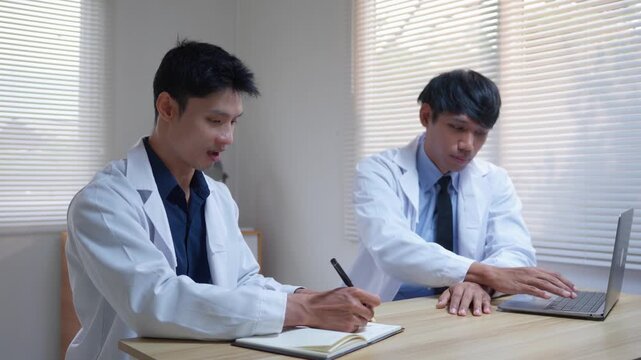 Two asian male doctors discussing a medical case and taking notes in a modern clinic office during a professional meeting