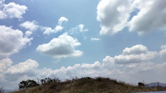 Vista en movimiento de un cielo azul con nubes blancas y follaje de &aacute;rboles a lo largo del camino.