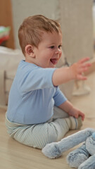 Fototapeta premium Toddler boy reaches with hand and sticks out tongue at plush rabbit while sitting on floor in a building; joy curiosity.