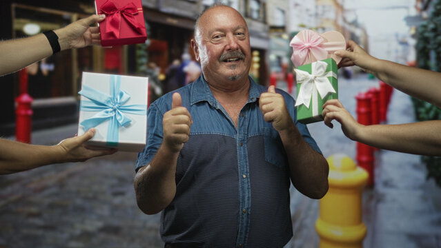Man gives thumbs up while multiple hands present wrapped gift boxes and bows beside exposed forearms on a cobbled shopping street; gratitude celebration joy.