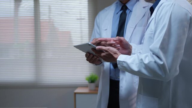 Two doctors using a digital tablet discussing patient medical records in a modern hospital office