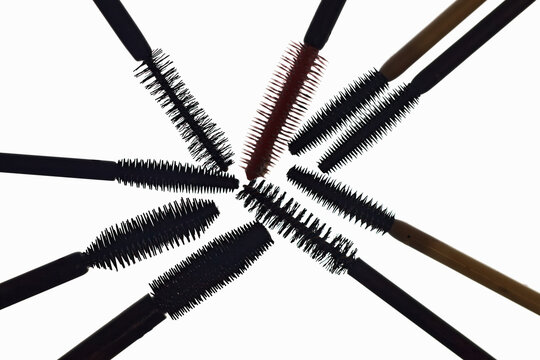 A composition of various mascara brushes arranged in  circular shape isolated on white background, showcasing different spoolie types, wand designs, and colors for makeup, beauty, and cosmetic concept