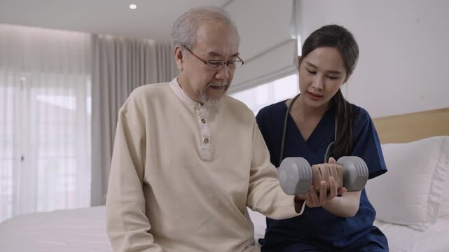 Professional Asian woman nurse physiotherapist using a dumbbell for workout exercise for physical recovery of muscles and bones of a senior man patient in hospital bed. Healthcare and medical concept.