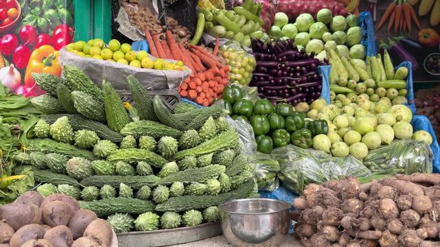 A vibrant stall piled high with bitter gourd, eggplants, carrots, and round gourds at a busy street market.